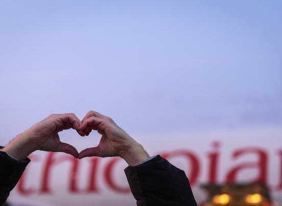 Une personne fait un coeur avec les mains devant un avion